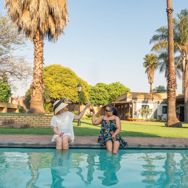 Photos of two ladies sitting with their legs in a pool at a hotel in Mpumalanga, and palm trees surrounding them.